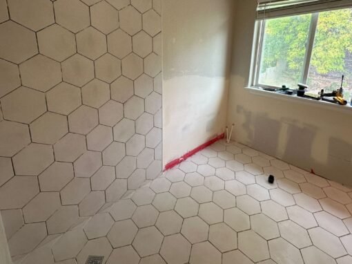 A collage of bathroom photos showcasing the installation of hexagonal tiles with grout. The images highlight different angles of the tiled floor and shower walls, displaying the even distribution of grout between the tiles, creating a smooth and professional finish. The light from a nearby window illuminates the bathroom, enhancing the contrast between the tiles and the newly applied grout.