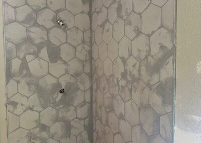 A collage of bathroom photos showcasing the installation of hexagonal tiles with grout. The images highlight different angles of the tiled floor and shower walls, displaying the even distribution of grout between the tiles, creating a smooth and professional finish. The light from a nearby window illuminates the bathroom, enhancing the contrast between the tiles and the newly applied grout.