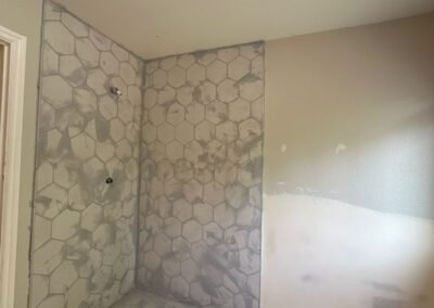 A collage of bathroom photos showcasing the installation of hexagonal tiles with grout. The images highlight different angles of the tiled floor and shower walls, displaying the even distribution of grout between the tiles, creating a smooth and professional finish. The light from a nearby window illuminates the bathroom, enhancing the contrast between the tiles and the newly applied grout.