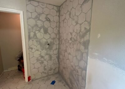 A collage of bathroom photos showcasing the installation of hexagonal tiles with grout. The images highlight different angles of the tiled floor and shower walls, displaying the even distribution of grout between the tiles, creating a smooth and professional finish. The light from a nearby window illuminates the bathroom, enhancing the contrast between the tiles and the newly applied grout.