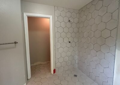 A collage of bathroom photos showcasing the installation of hexagonal tiles with grout. The images highlight different angles of the tiled floor and shower walls, displaying the even distribution of grout between the tiles, creating a smooth and professional finish. The light from a nearby window illuminates the bathroom, enhancing the contrast between the tiles and the newly applied grout.