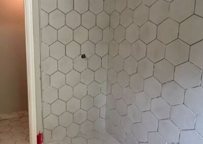 A newly tiled shower and bathroom floor featuring large hexagon tiles. The clean, geometric pattern covers both the wall and floor, creating a modern, cohesive look. The grout lines are visible, and the installation is nearing completion with finishing touches still to be applied.