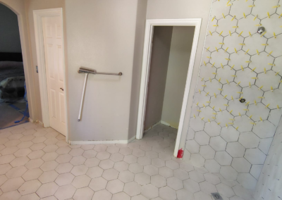 Close-up view of a hexagonal tile floor in a bathroom before grout application. The tiles are evenly spaced, and the preparation phase is visible, with unfinished areas showing where grout will be applied. Light from a nearby window casts shadows across the clean, new tile surface, emphasizing the hexagonal pattern.