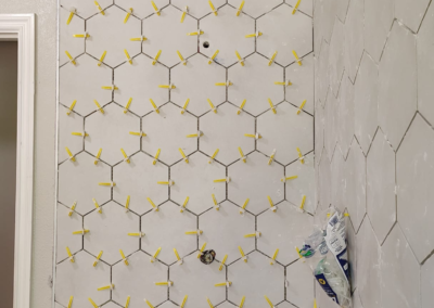 Close-up view of a hexagonal tile floor in a bathroom before grout application. The tiles are evenly spaced, and the preparation phase is visible, with unfinished areas showing where grout will be applied. Light from a nearby window casts shadows across the clean, new tile surface, emphasizing the hexagonal pattern.