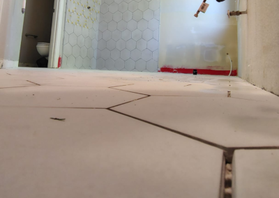 Close-up view of a hexagonal tile floor in a bathroom before grout application. The tiles are evenly spaced, and the preparation phase is visible, with unfinished areas showing where grout will be applied. Light from a nearby window casts shadows across the clean, new tile surface, emphasizing the hexagonal pattern.